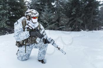 Winter arctic mountains warfare. Action in cold conditions. Trooper with weapons in forest somewhere above the Arctic Circle on one knee
