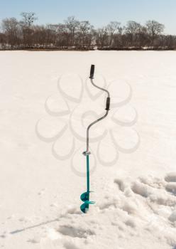 Fishing auger on an ice of the frozen river