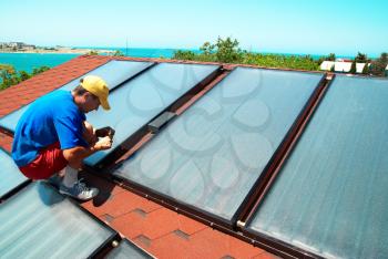 Worker mounting solar water heating panels on the roof.