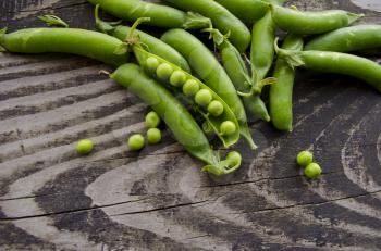 Vintage wooden surface for design with beautifully pods of green peas. Young fresh green peas on old wooden background. Agriculture, gardening, harvest, healthy lifestyle concept.