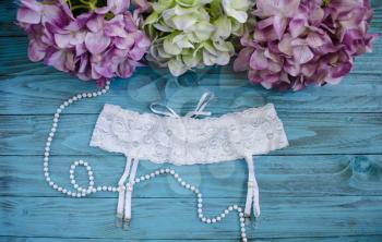White belt for stockings with lace. Lingerie, isolate on a blue wooden background with hydrangea flowers.