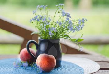 Still life with wildflowers and peaches. Flowers in vase with peach fruit on a table in a summer cottage