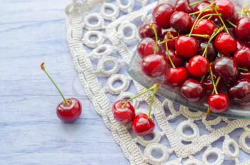 Fresh ripe cherries on wooden table. Cherries in a transparent glass plate and kitchen napkin.