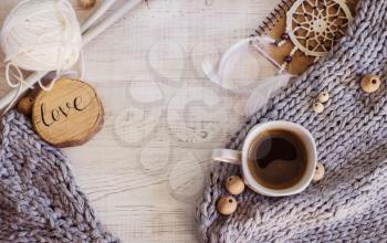 Cozy composition with coffee, knitted elements from merino wool on a wooden background. A photo in a Hygge style.