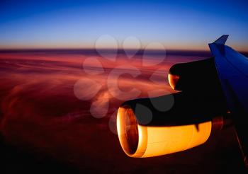 View of the sunset from the airplane porthole. The view from the window of a passenger plane during the flight, the wing of the turbine engine of the aircraft.