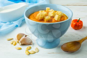 Pumpkin squash vegetable soup with garlic croutons in a blue bowl on white wooden background