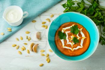 Creamy pumpkin Squash vegetable soup topped with cream in a turquoise plate, pumpkin seeds, garlic and parsley, top view 