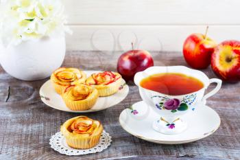 Cup of tea and muffins with rose shaped apple slices. Sweet apple dessert pie. Homemade apple rose pastry. Breakfast tea with sweet apple pastry 
