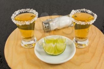 Shots of gold tequila with lime and salt on the wooden tray. Gold Mexican tequila. Tequila. Tequila shot.