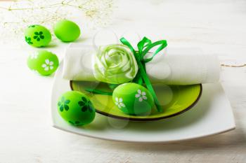 Green Easter table place setting with plate, napkin and Green Decorated Easter eggs on white wooden background