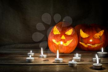 Halloween symbol pumpkin smiling jack-o-lantern and burning candles on dark wooden background, horizontal, copyspace