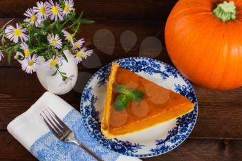 Thanksgiving pumpkin pie slice on plate, linen napkin, vase, lilac flowers on a wooden background