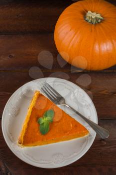 A piece of pumpkin pie with mint, white plate, fork on dark wooden background vertical
