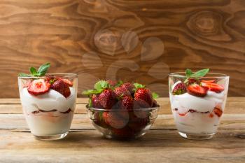 Strawberries dessert with whipped cream on rustic wooden background. Cream cheese  layers and ripe strawberry.