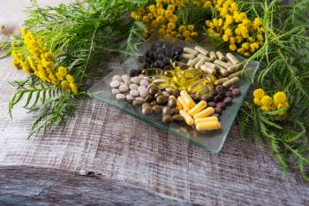 Ayurvedic herbal pills on the glass plate and tansy yellow flowering plant. Healthy life concept