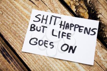 Shit happens but life goes on handwritten message on white paper with retro wooden bark background. Motivational handwritten message on paper with retro background.