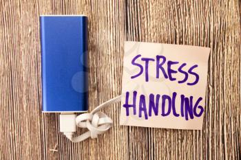 Stress Handling is presented on note paper in black color. Energy storage device of blue color with cable on wooden background. This picture is dealing Stress in different conditions Concept.