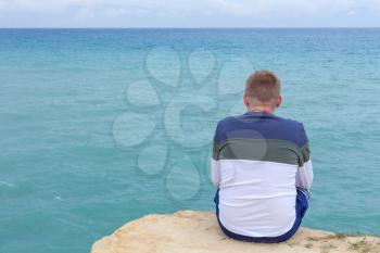 Man sitting on the cliff. Tourist ovelooking the open sea. Waves shoaling and approcahing the seabed.Relaxing tropical destination. Sightseeing and outdoor unwinding activity