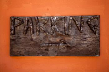Parking sign. Rustic wooden boards with engraved letters and arrow in orange wall. Indication to public space to park vehicles. Directions. Carved wood signs