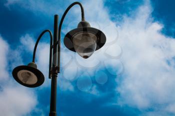 Light post with two bulbs and blue cloudy sky background. Outdoor street lights. Cast iron lamp. Large lanterns. Lighting pole. Illuminate. Electrical device