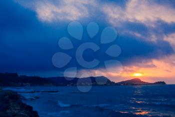 Sunset Sea Perspective from the Shoreline, Beautiful Mountain Ocean view Landscape, Shimmering Twilight with blue and dark colors, Hidding Sun between Cloudy Sky