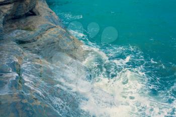 Bright Blue Ocean Surface with Waves and Foaming crashing againts the natural clay wall, Dark Turquoise Water Waving at the pace of the Breeze, Mediterranean Sea Landscape View from the Sky