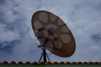 Round television satellite dish above bricked roof. Facing the cloudy blue sky. Giving clear reception of television in living room where it is situated. 