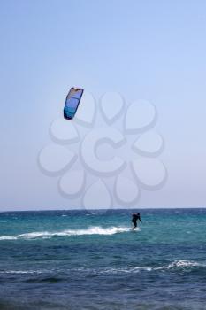 A black vested kitesurfer is using  blue coloured inflatable kite on relatively quite turqouise sea. Inflatable kites are popular in many year in kite surfing because of its reliability.