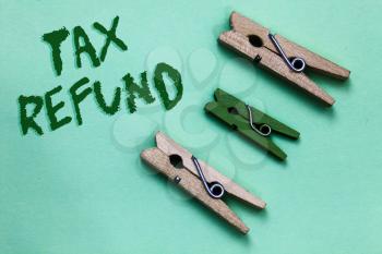Text sign showing Tax Refund. Conceptual photo applied when money liability is less than the paid ones Three brown green vintage clothespins clear background Holding things
