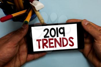 Conceptual hand writing showing 2019 Trends. Business photo showcasing things that is famous for short period of time in current year Man holding cell phone looking messages apps cup markers