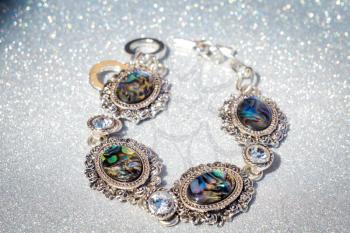 Fashion retro silver bracelet decorated with dark rainbow abalone shell on glitter background.