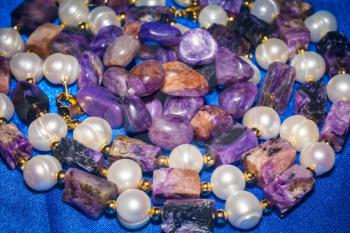 Necklace and bracelet made of natural charoite and pearls background.