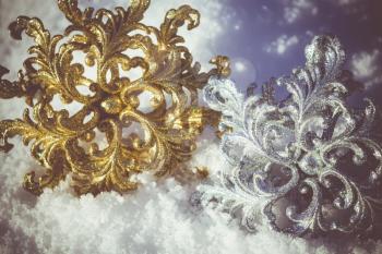 Ornamental golden and silver snowflake glittering on fresh white snow, filtered colors.