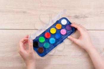 Hand holding a watercolor paint box on a wooden background