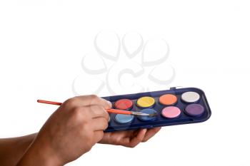 Child holding a watercolour paint set and a brush in his hand