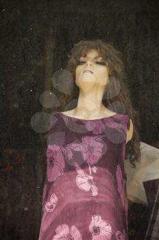 Plastic mannequin doll behind the dusty window of an abandoned store.