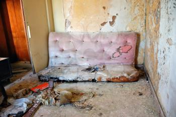 Broken couch and peeling paint wall. Abandoned house interior.