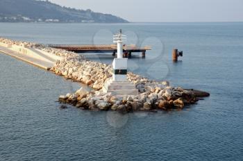 utomated lighthouse by the sea and rock jetty breakwater at port entrance.