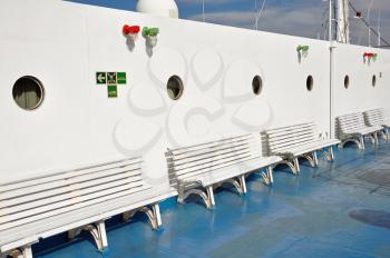 Row of benches and portholes on ship deck painted with white and blue colors.