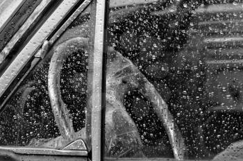 Vintage car interior through rain covered window steering wheel wrapped in plastic. Black and white.