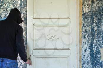 Man opening door of decayed room with torn floral wallpaper imprint on the wall.