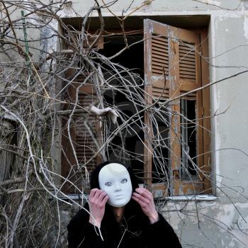 Grotesque white mask figure and haunted house window with tangled overgrown plants and creepy dummy doll hand.
