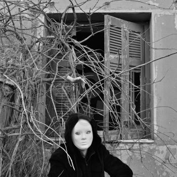 Masked figure and cut hand creeping though overgrown branches at haunted house.