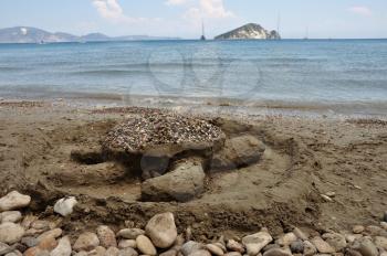 Loggerhead sand sculpture on Keri beach and distant view of Marathonisi islet shaped like a gigantic sea turtle and favorite nesting ground of the caretta caretta. Zakynthos, Greece.