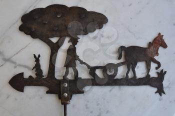 Rusty weather vane with pastoral scene farmer ploughing with horse. Vintage metal architectural ornament for showing wind direction.