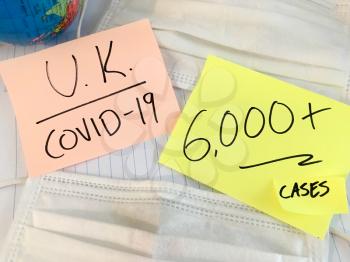 UK Coronavirus COVID-19 infection medical cases and deaths United Kingdom. China COVID respiratory disease influenza virus statistics hand written on surgical mask and earth globe background