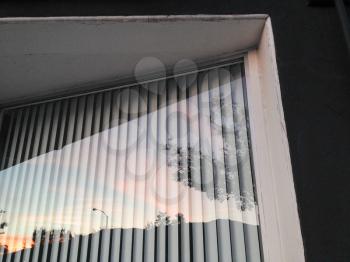 Glass window reflection of sunset with vertical blinds and mountain horizon clouds