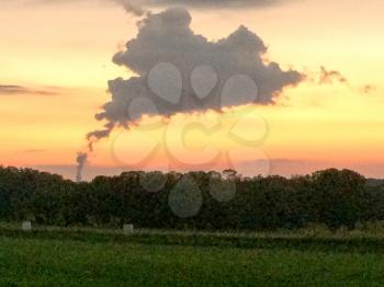 sunset over green grassy farm field with strange cloud of steam amoke