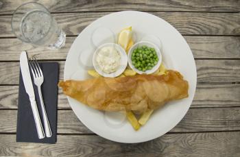 Fish and chips served with tartar sauce, green peas and lemon on a rustic background