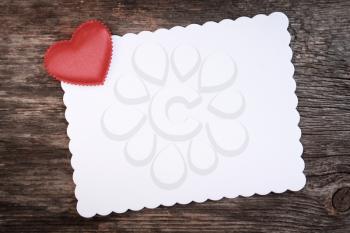Red heart on blank white paper cardboard invitation on a wooden background.